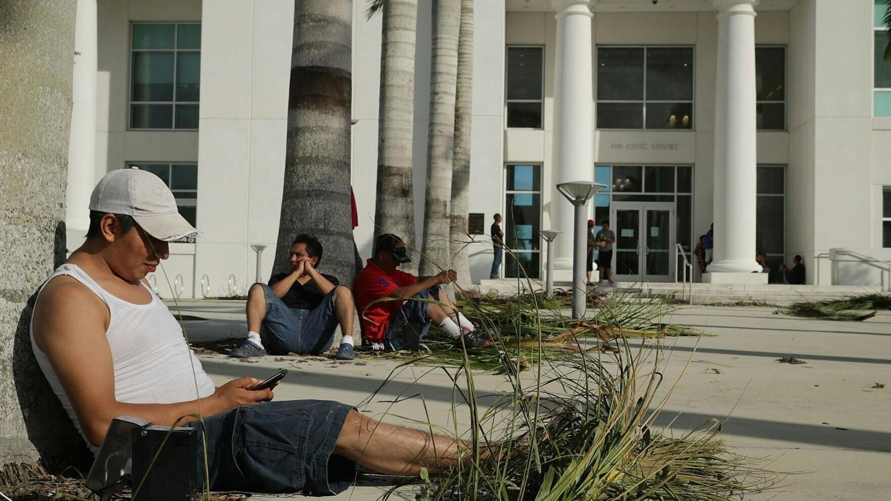 Residents without power at home charge their mobile phones using electrical outlets at the base of palm trees at City Hall in Homestead, Fla., after Hurricane Irma in September 2017.
              Chip Somodevilla/Getty Images