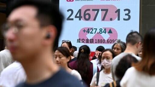 Pedestrians walk next to an electronic sign board showing the Hang Seng Index in Hong Kong