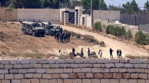 Israeli soldiers stand guard next to settlers in front of Palestinian houses in the village of Qusra, south of Nablus, in the occupied West Bank