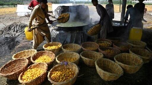 Muhammad Idrees (L) ladles boiled dates from a vat simmering over an open flame, work that labourers lament is getting hotter each year in Pakistan