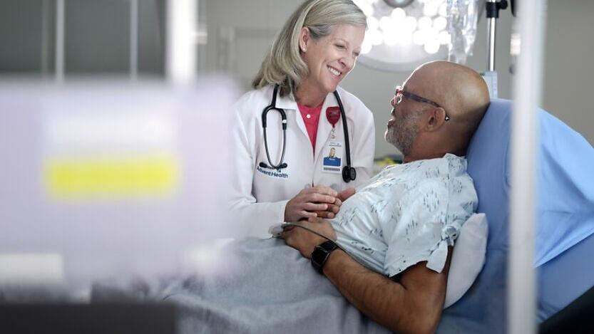 A physician at AdventHealth Tampa holds the hand of a patient in the emergency room.