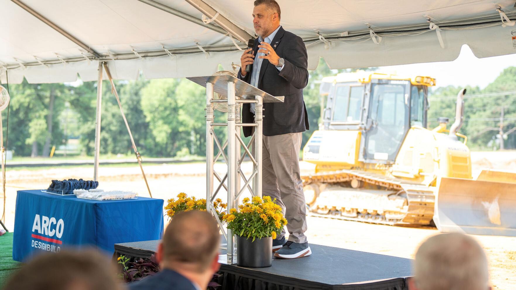 A representative addresses attendees at the OPW groundbreaking ceremony in Smithfield, North Carolina, with earthmoving equipment staged in the background ahead of construction on the new manufacturing facility.