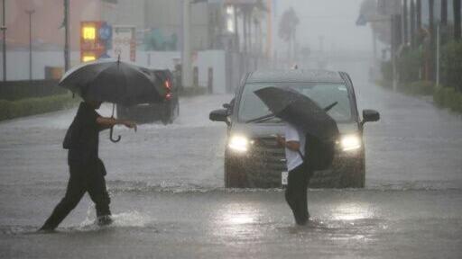 People wade through a flooded road as heavy rain falls amid weather patterns due to Typhoon Dujuan in Funabashi, Chiba Prefecture on September 21, 2026.