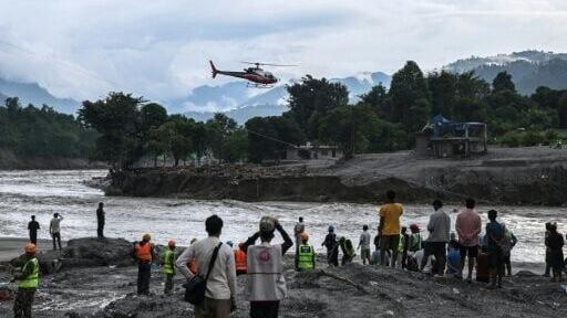 A rescue helicopter flies as Army personnel and members of Nepal Scouts install a zip-line across the Trishuli River in the aftermath of flash floods