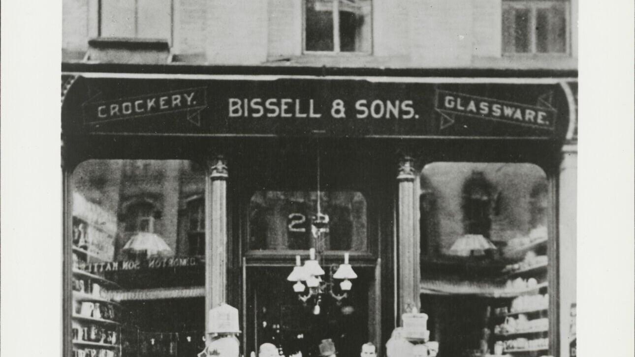 Black and white photograph print of the Bissell &amp; Sons Crockery and Glassware Storefront, from the BISSELL Building History Scrapbook, 1876.
