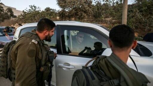 Israeli soldiers watch as US-Palestinian dual citizen Louai Abu Ridi, whose home in the Israeli-occupied West Bank village of Qusra is besieged by Israeli settlers, arrives by car to visit his mother at her home in the same village