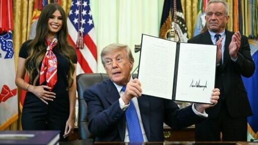 US President Donald Trump holds up his vaccine order with (right) Health Secretary Robert F. Kennedy Jr.