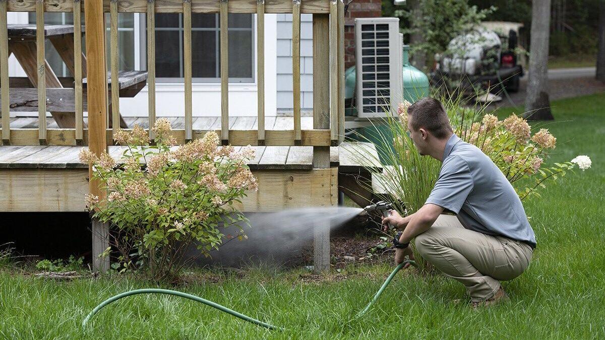 ohDEER technician applying all-natural tick and mosquito control beneath a deck in the backyard of a home.