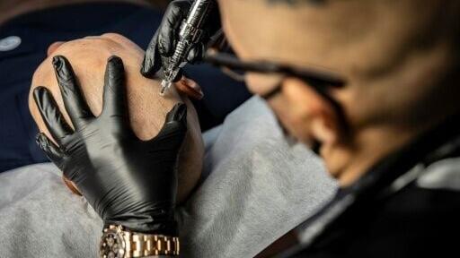 Tattoo artist Remy performing a scalp micropigmentation procedure on client Koki Hatanaka at his studio in Ginowan