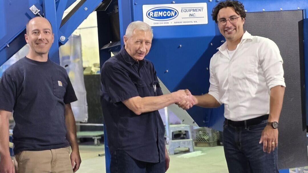 Dan, Dennis, and Sean shake hands in front of the Remcon Material Separation Unit that includes an eddy current and an air knife