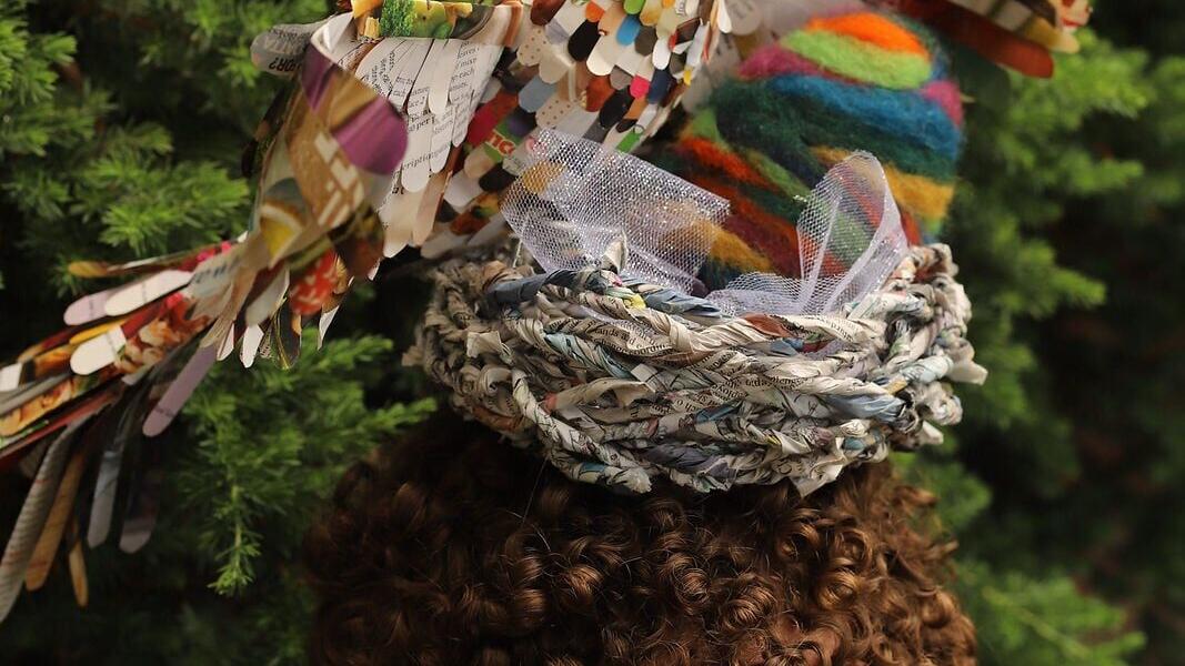 A student wears a handmade headpiece featuring a colorful bird and nest constructed from recycled paper and other mixed materials.