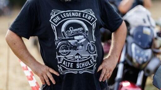 A man at an AfD campaign event wears a T-shirt showing a Simson moped and the words 'the legend lives, old school'