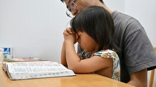 Ren Zhong, the husband of detained pastor Wang Cong, reads a copy of the Bible and prays with his daughter Huanle at their house in Beihai, southern China's Guangxi province