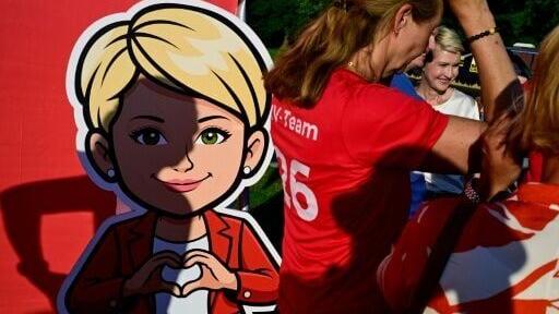 A campaign comic figure depicts Schwesig forming a heart with her hands